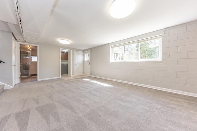 unfurnished living room with baseboards, stairway, light colored carpet, washer / dryer, and concrete block wall