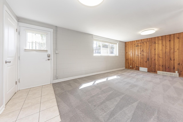 unfurnished room featuring light carpet, visible vents, wood walls, and concrete block wall