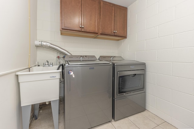 laundry area with a sink, washing machine and dryer, cabinet space, concrete block wall, and light tile patterned floors