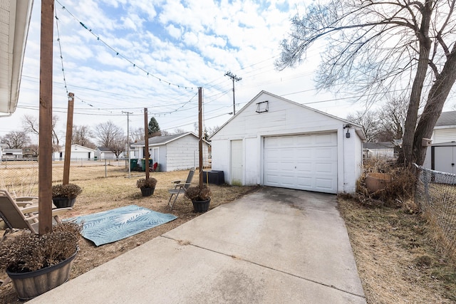 detached garage featuring concrete driveway and fence