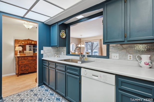 kitchen featuring white dishwasher, a sink, decorative backsplash, light countertops, and blue cabinets