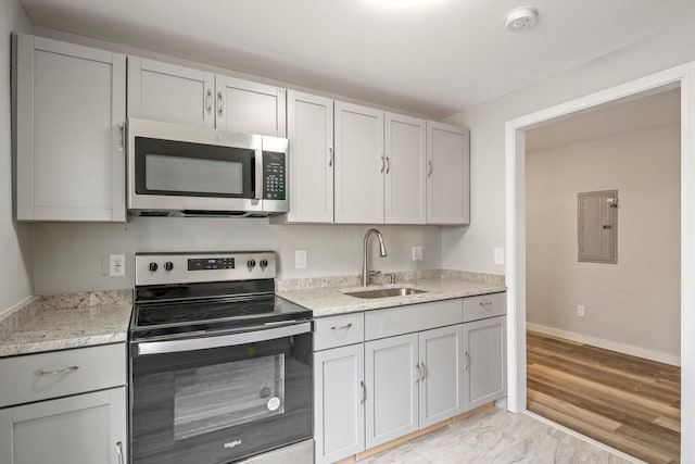 kitchen with light stone countertops, electric panel, a sink, gray cabinetry, and stainless steel appliances