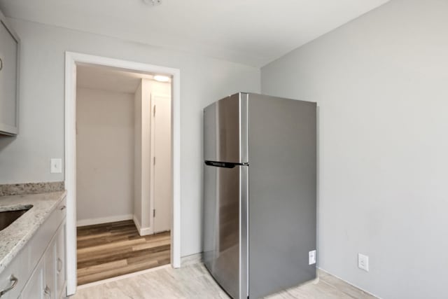 kitchen with light wood finished floors, baseboards, light stone countertops, freestanding refrigerator, and white cabinets