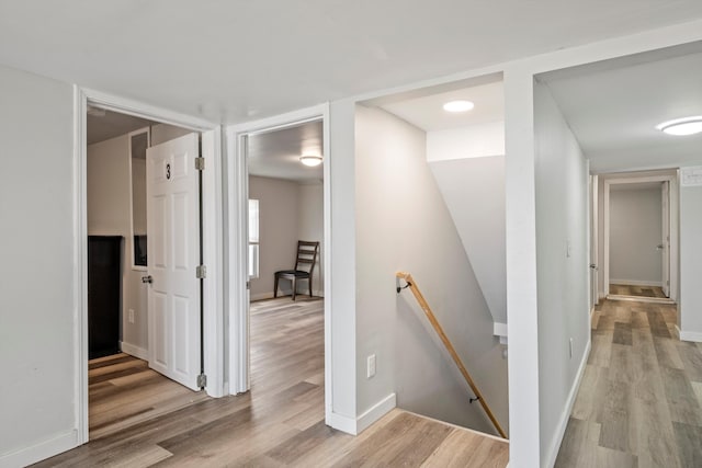 hall featuring light wood-type flooring, an upstairs landing, and baseboards