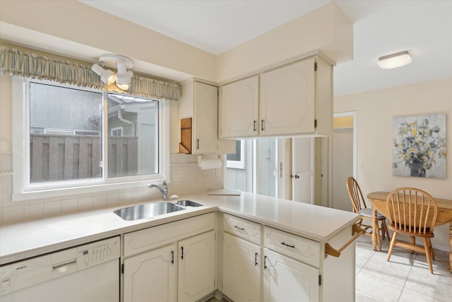 kitchen with a sink, backsplash, a peninsula, white dishwasher, and light countertops