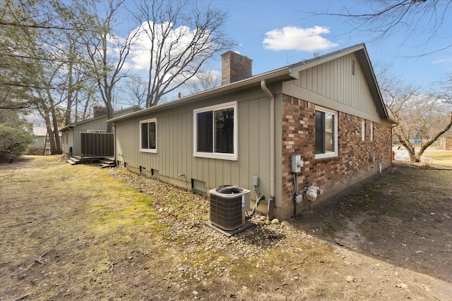 exterior space featuring brick siding, central air condition unit, and a chimney