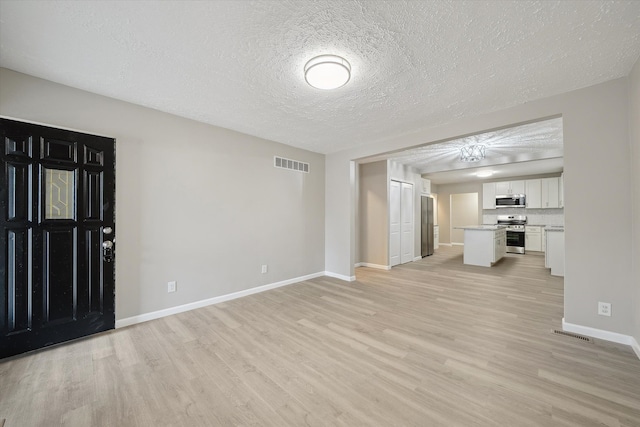 unfurnished living room featuring light wood-type flooring, visible vents, baseboards, and a textured ceiling