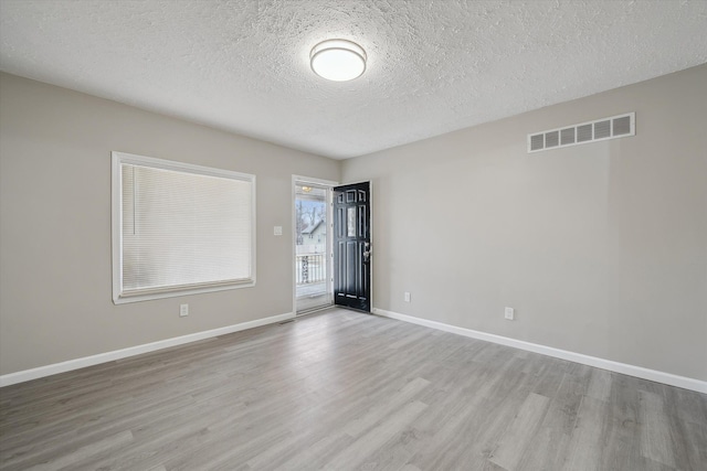 spare room with visible vents, a textured ceiling, baseboards, and wood finished floors