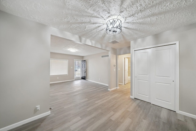 interior space featuring visible vents, baseboards, a textured ceiling, and wood finished floors