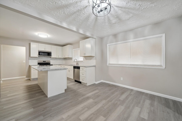 kitchen with light wood finished floors, a sink, white cabinets, appliances with stainless steel finishes, and a center island