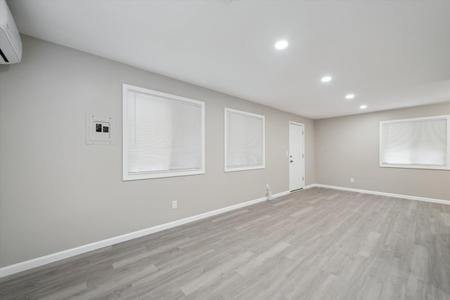 spare room featuring recessed lighting, baseboards, a wall mounted air conditioner, and light wood-type flooring