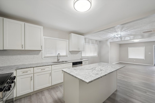 kitchen featuring visible vents, a kitchen island, light wood-style flooring, a sink, and appliances with stainless steel finishes