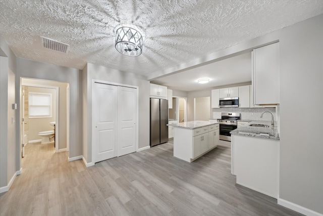 kitchen featuring visible vents, light wood-style flooring, white cabinets, appliances with stainless steel finishes, and a center island