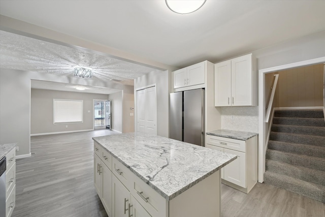 kitchen with a kitchen island, light stone counters, light wood-style floors, white cabinets, and stainless steel appliances