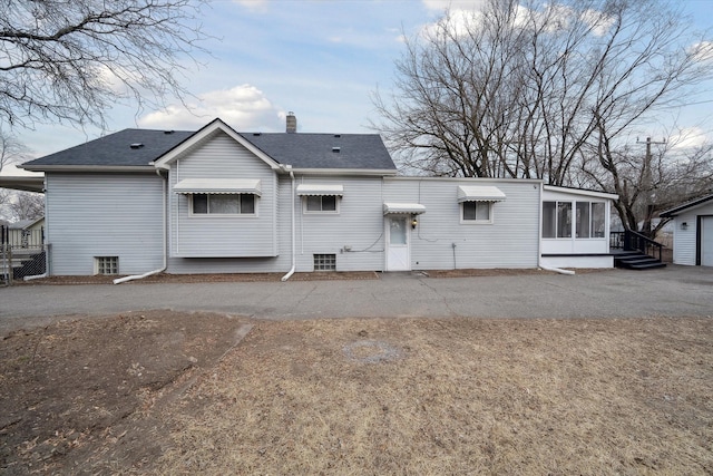 back of property with a chimney, roof with shingles, and a sunroom