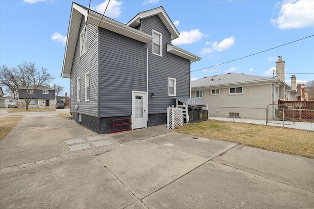 back of property featuring a lawn, concrete driveway, and fence