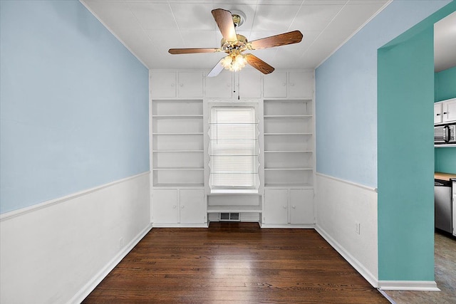 empty room with ornamental molding, a ceiling fan, built in features, wood finished floors, and baseboards