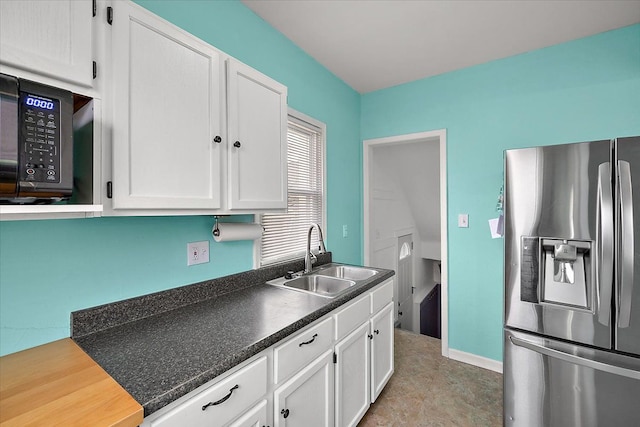 kitchen with stainless steel fridge, white cabinetry, black microwave, and a sink