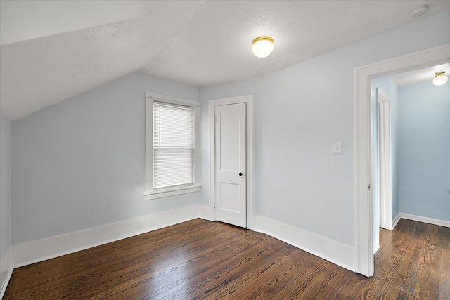 additional living space with a textured ceiling, baseboards, lofted ceiling, and dark wood-style flooring