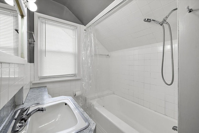 bathroom with vaulted ceiling, tile walls, shower / bath combo, and a sink