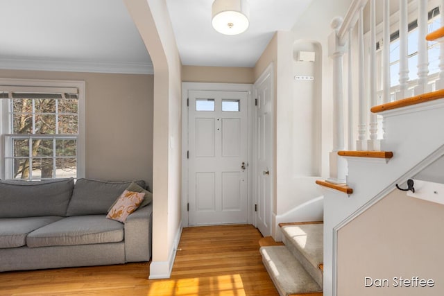 foyer entrance featuring light wood-type flooring, ornamental molding, arched walkways, baseboards, and stairs