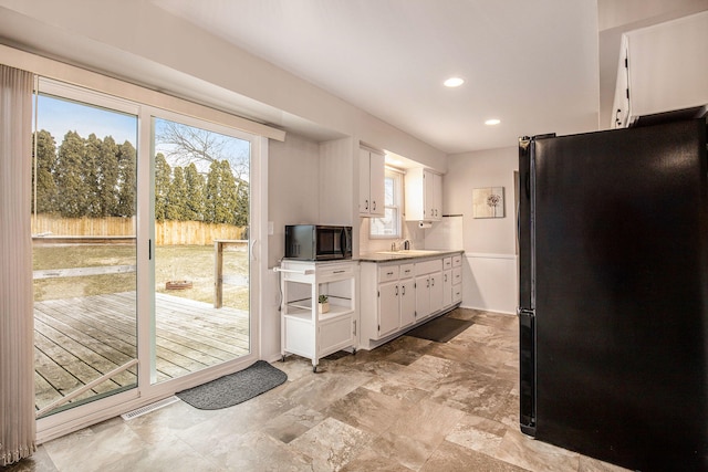 kitchen with stainless steel microwave, white cabinetry, recessed lighting, freestanding refrigerator, and light countertops