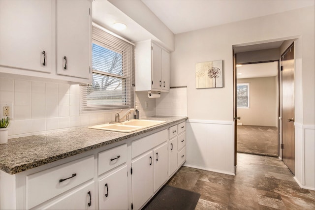 kitchen featuring decorative backsplash, white cabinets, wainscoting, and a sink