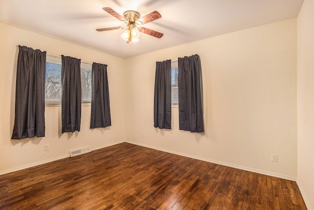 spare room featuring a wealth of natural light, visible vents, a ceiling fan, and dark wood-style flooring