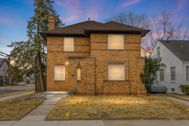 traditional home with brick siding, a lawn, a chimney, and a shingled roof