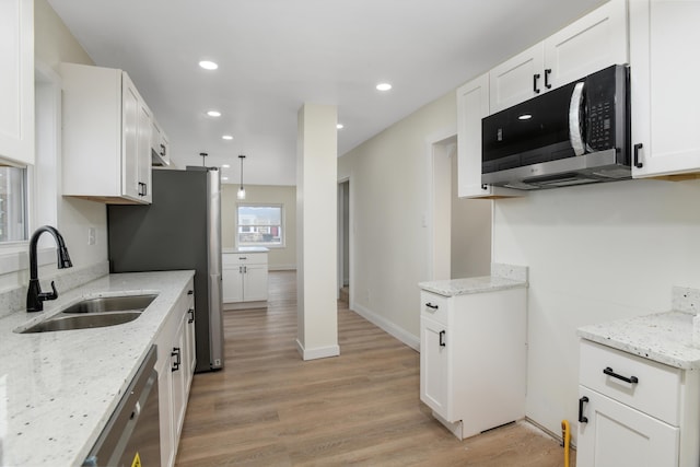 kitchen featuring light stone counters, light wood-style flooring, stainless steel appliances, and a sink