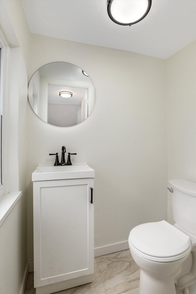 half bath with baseboards, toilet, marble finish floor, and vanity