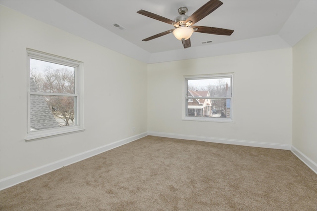 empty room featuring a raised ceiling, carpet, visible vents, and baseboards