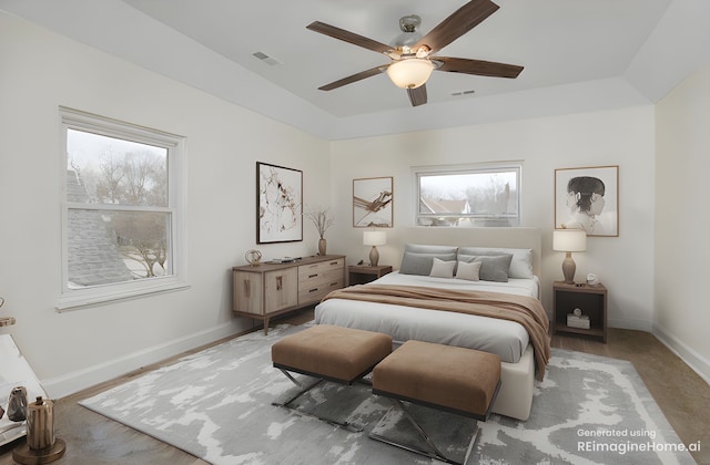 bedroom with a tray ceiling, visible vents, baseboards, and a ceiling fan