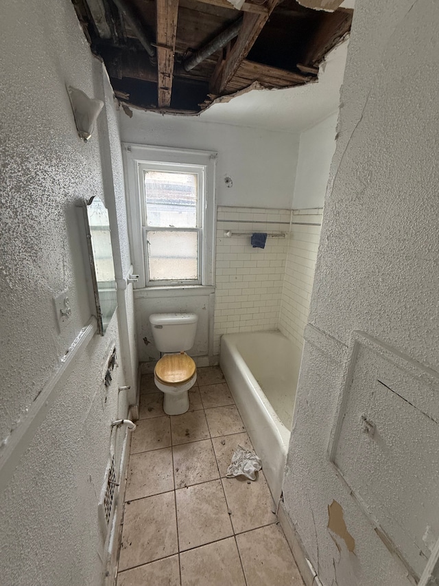 bathroom featuring tile patterned flooring, toilet, a textured wall, and shower / bath combination