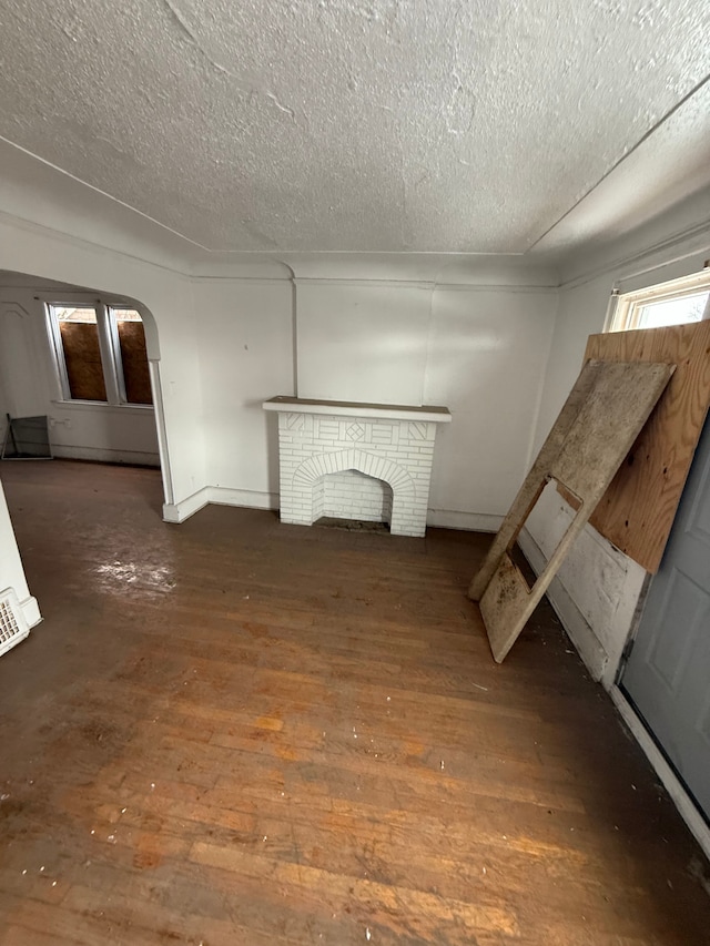 unfurnished living room featuring arched walkways, a textured ceiling, a brick fireplace, and hardwood / wood-style flooring