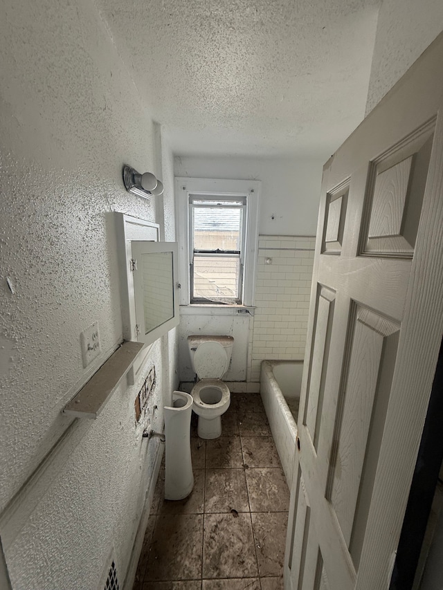 bathroom featuring a bathtub, a textured ceiling, toilet, and a textured wall