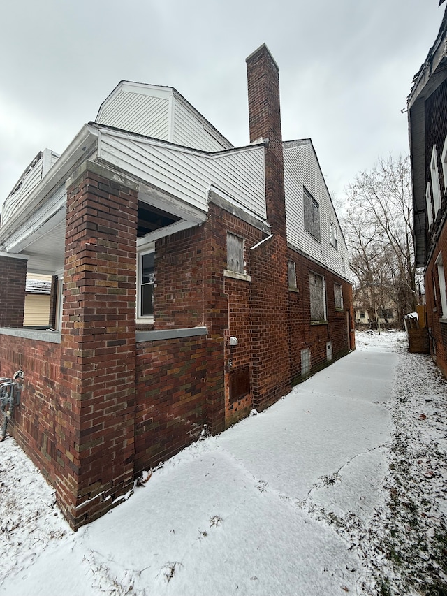 view of snowy exterior featuring brick siding and a chimney