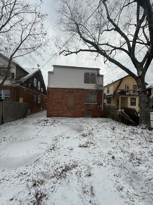 snow covered house with brick siding and fence