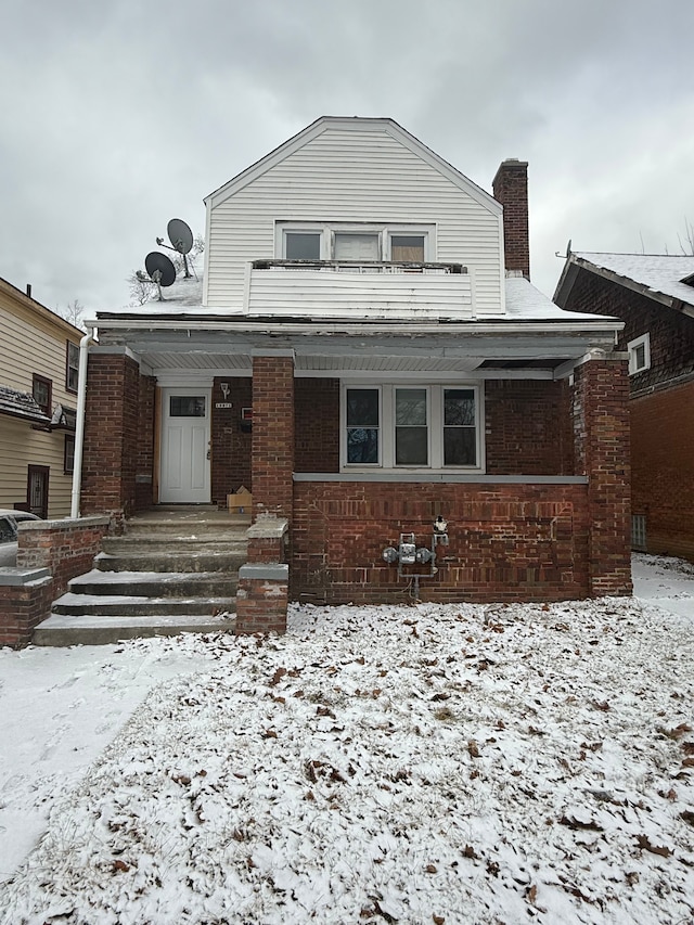 view of front facade with brick siding, a porch, and a chimney