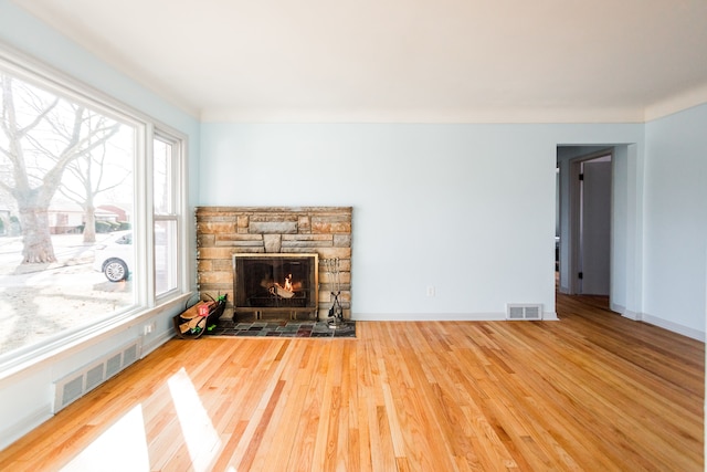 living area with a stone fireplace, baseboards, visible vents, and wood finished floors