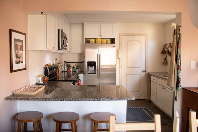 kitchen featuring backsplash, dark stone countertops, appliances with stainless steel finishes, a peninsula, and white cabinetry