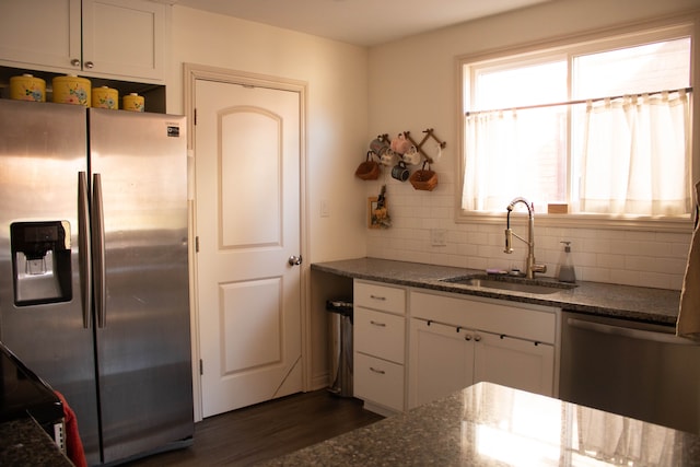 kitchen with backsplash, dark stone countertops, white cabinets, stainless steel appliances, and a sink