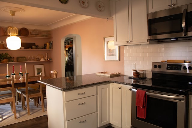 kitchen with dark stone countertops, a peninsula, stainless steel appliances, white cabinets, and backsplash