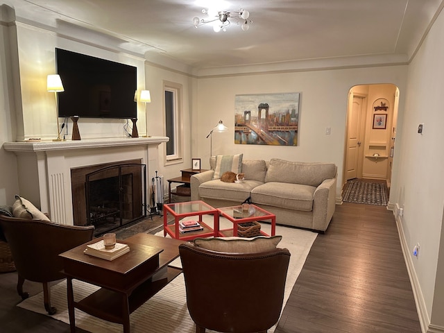 living room featuring a fireplace with flush hearth, ornamental molding, hardwood / wood-style floors, arched walkways, and baseboards