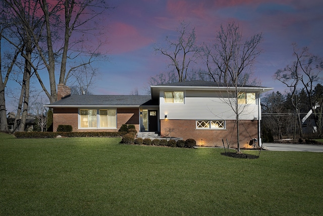 split level home with a yard, brick siding, and a chimney