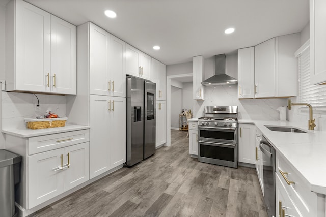 kitchen featuring light wood-type flooring, a sink, backsplash, stainless steel appliances, and wall chimney range hood