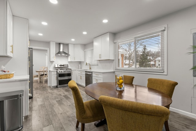 kitchen featuring light wood finished floors, stainless steel appliances, light countertops, white cabinets, and wall chimney exhaust hood