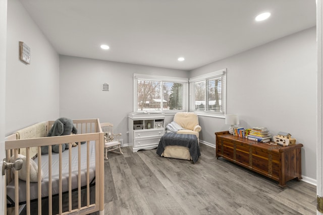 bedroom with recessed lighting, a nursery area, and wood finished floors