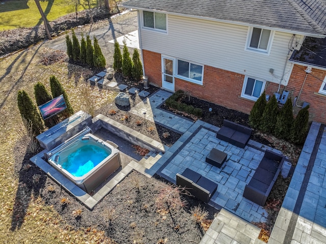 exterior space featuring a jacuzzi, a patio area, brick siding, and roof with shingles