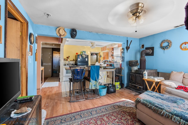 living room with visible vents, a wood stove, a ceiling fan, and wood finished floors